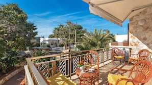 A balcony with wicker furniture, a table with a vase of flowers, and a view of the street and buildings. - 3214 Villa Serenè - Appartamento A by Barbarhouse (Racale)