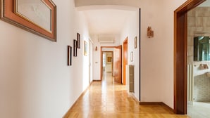 A hallway with hexagonal patterned flooring, framed artwork on the walls, and a wooden door leading to a bathroom. - 3214 Villa Serenè - Appartamento A by Barbarhouse (Racale)