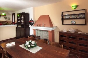 Un comedor con mesa de madera, sillas, chimenea, estantería y repisa con platos decorativos.
