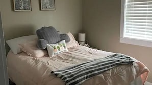 Ein ordentlich gemachtes Bett mit einer gestreiften Decke, einem Kissen mit Pflanzenmuster und zwei Wandbildern.