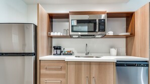 A modern kitchen with a stainless steel refrigerator, microwave, and dishwasher, wooden cabinets, and a white countertop.