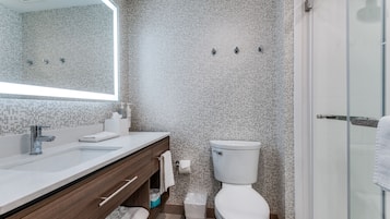 A modern bathroom with a large mirror, a white sink, a toilet, and a shower area.