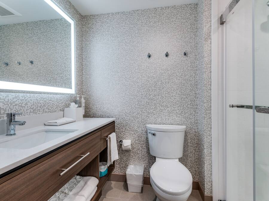 A modern bathroom with a large mirror, a white sink, a toilet, and a shower area.