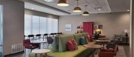 A modern lounge area with a green sofa, round tables, and chairs.
