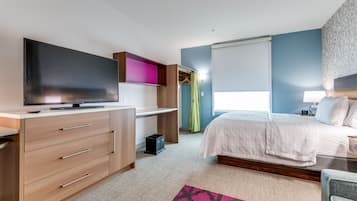 A bedroom with a bed, a desk with a flat-screen TV, a wardrobe, and a window with curtains.