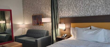 Una habitación de hotel con una cama, una silla, una mesita de noche con teléfono, una lámpara y un espejo.