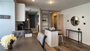 Une cuisine moderne dotée d’un îlot central intégré, d’un coin repas avec une table en bois foncé et des chaises recouvertes d’un tissu gris, ainsi que d’un garde-manger.