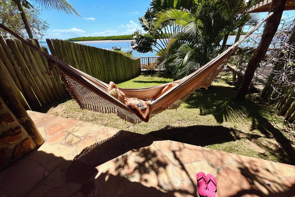 Una hamaca en un patio trasero con un muro de piedra, una valla de madera y vista al mar.