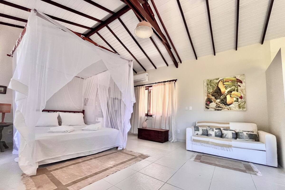 Un dormitorio con cama con dosel, un sofá, un cuadro y suelo de baldosas.