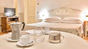 A neatly arranged breakfast table with a coffee maker, cups, and a pitcher, set against a bedroom with a bed and a television in the background. - Residence con piscina a Monteverdi  (Monteverdi Marittimo)