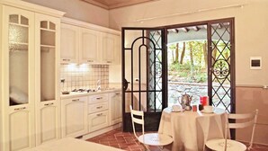 A kitchen with white cabinets, a dining table with chairs, and a view through a glass door. - Residence con piscina a Monteverdi  (Monteverdi Marittimo)