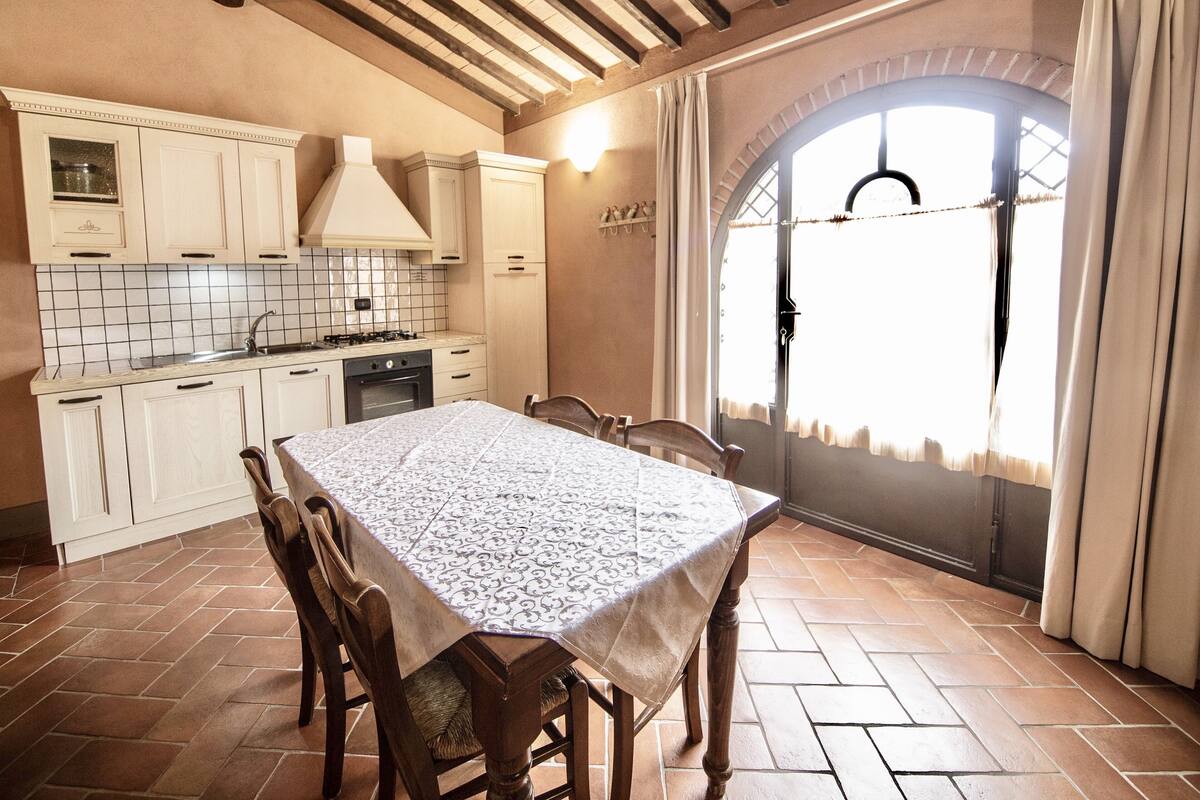 Een keuken met witte kastjes, een betegelde achterwand en een eettafel met stoelen.