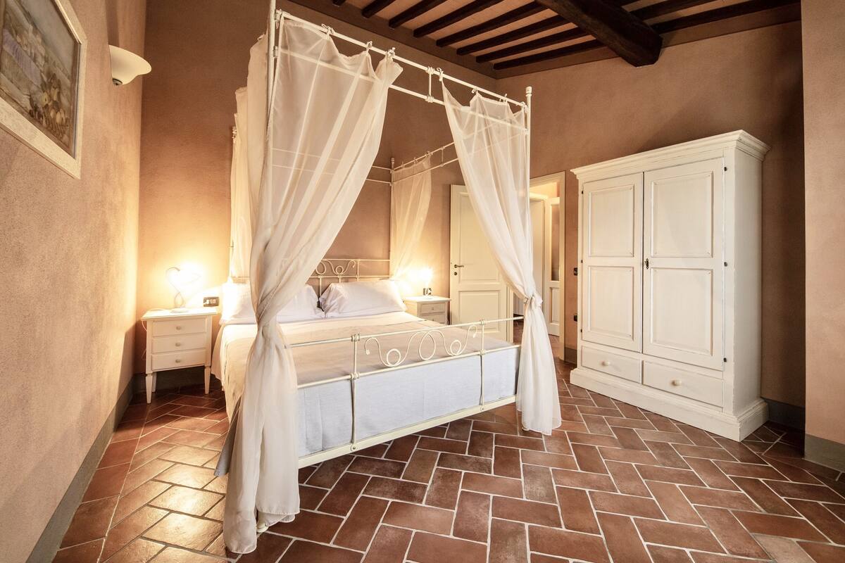 Een slaapkamer met een hemelbed, een witte inloopkast en een betegelde vloer.