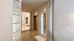 A modern hallway with a glass door leading to a bathroom, a glass shelf with decorative items, and a white mat on the floor. - Residence con piscina a Monteverdi  (Monteverdi Marittimo)