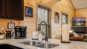 A kitchen with granite countertops, a coffee maker, a kettle, and a large white candle. - New Build! Hot Tub, Fireplace (Pigeon Forge)