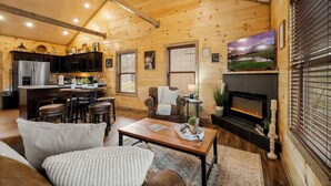 A cozy log cabin interior with a dining area, kitchen, and living room. - New Build! Hot Tub, Fireplace (Pigeon Forge)