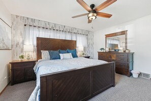 A bedroom with a bed, wooden headboard, nightstands, a dresser, a ceiling fan, and a large mirror.