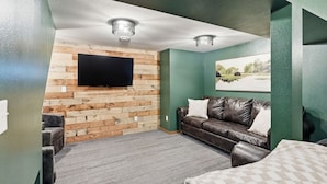 Een kamer met een flatscreen televisie aan een houten wand, een leren bank en een vloerkleed.