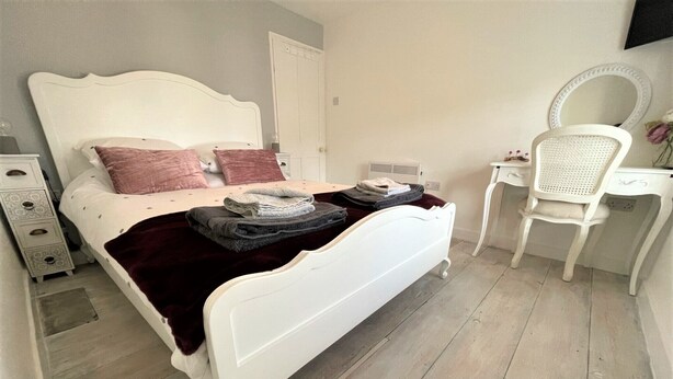 Un dormitorio con una cama blanca, un escritorio, una silla y un aparador.