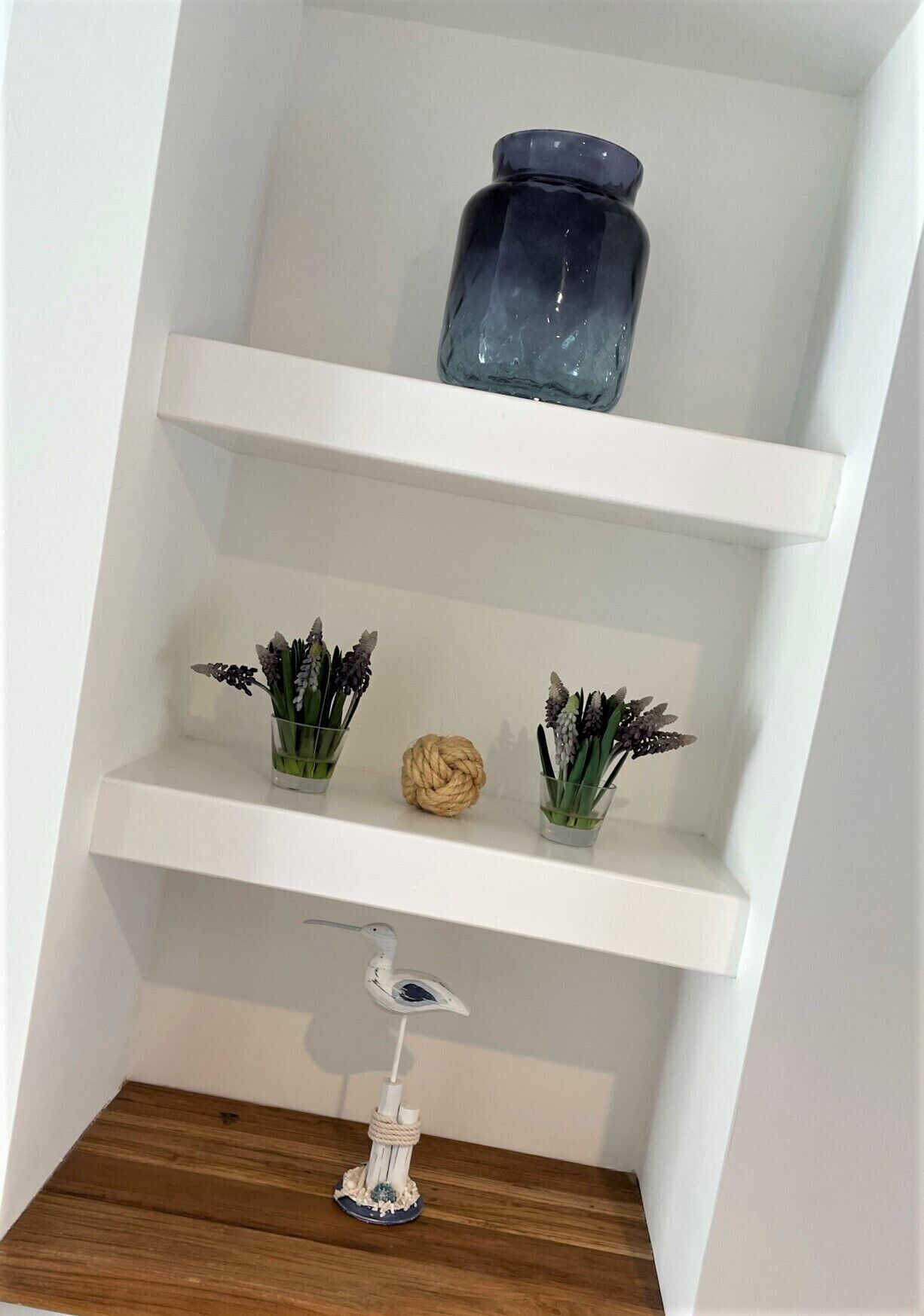 A white shelf with a blue vase, two glass containers with plants, and a decorative item on a wooden surface.