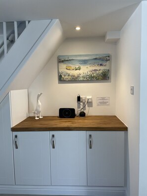 A room with a wooden counter, white cabinets, a painting of a beach scene, and a white sculpture.