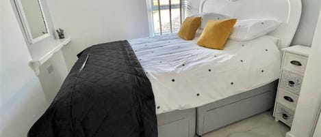Un dormitorio con cama, mesita de noche, cómoda, ventana con persianas y espejo montado en la pared.