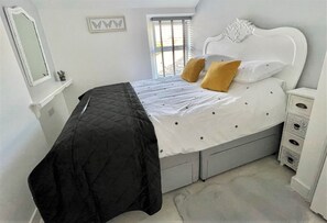 Un dormitorio con cama, ventana, cómoda y espejo.
