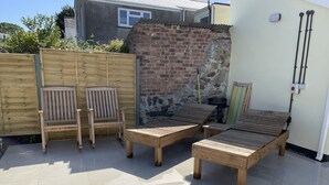 Un patio con mobiliario de madera, incluyendo dos sillas y dos sillones reclinables, un muro de ladrillo y suelo de baldosas.