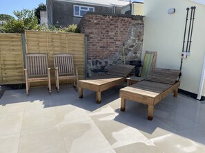 Un espace patio aménagé avec du mobilier en bois, comprenant deux chaises et deux fauteuils de relaxation, un mur en briques et un sol carrelé.