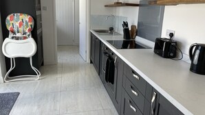 Una cocina moderna con armarios oscuros, una encimera blanca, un tostador, una tetera y una silla alta infantil de colores.