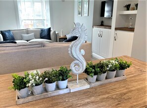 Una sala de estar con un sofá, una escultura decorativa de caballito de mar y una fila de plantas en macetas sobre una mesa de madera.
