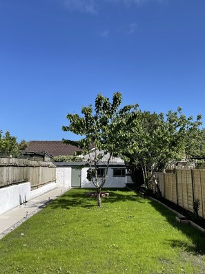 A backyard with a tree, a white house, and a wooden fence. - The Little Seahorse - Newly renovated near beach (Par)