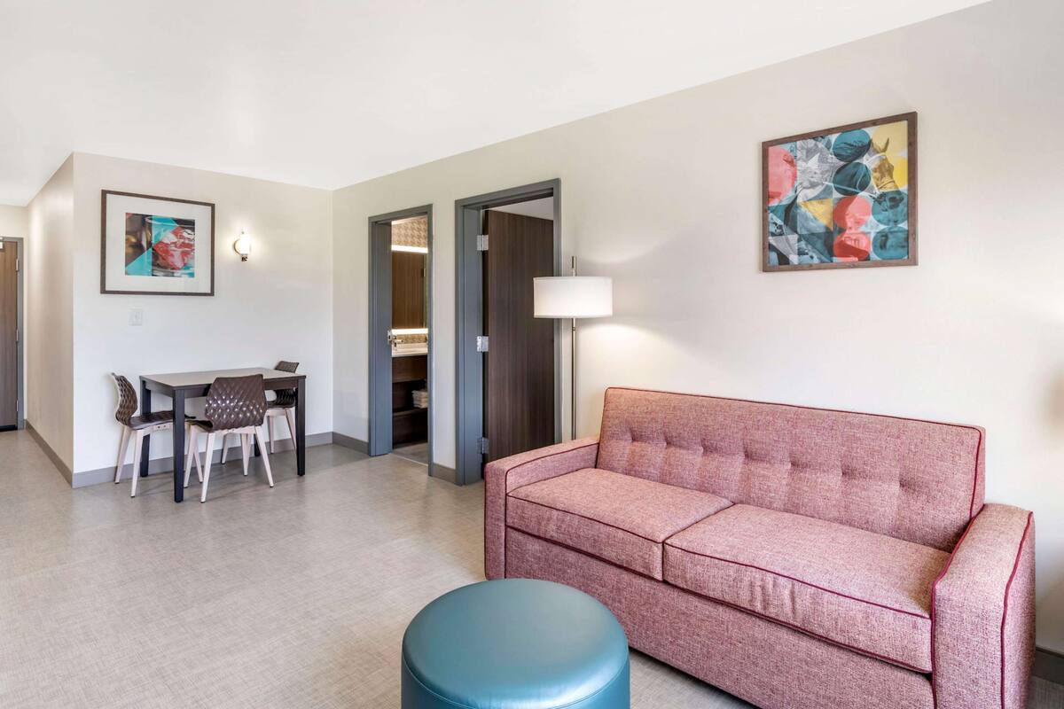 Un salon moderne avec un canapé, une table à manger et des chaises, ainsi qu’un pouf bleu.