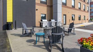 Ein Terrassenbereich im Freien mit Adirondack-Stühlen, einem blauen Tisch und einem Grill.