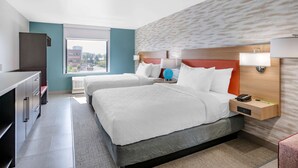 Ein Hotelzimmer mit zwei Betten, einem Schreibtisch und einem Fenster mit Blick auf die Stadt.