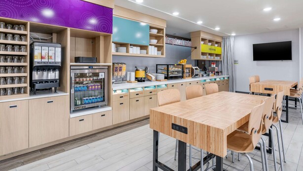 Ein modernes Café mit Holzkubaturen, einer Selbstbedienungsgetränkeausgabe und einem Flachbildfernseher an der Wand.