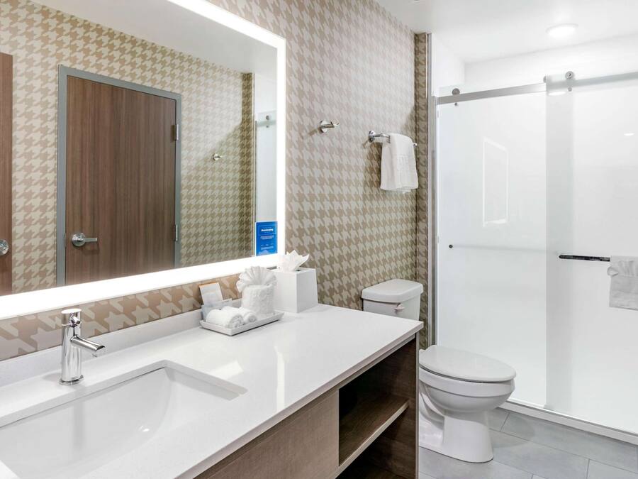 A modern bathroom with a large mirror, a sink, a toilet, and a shower.
