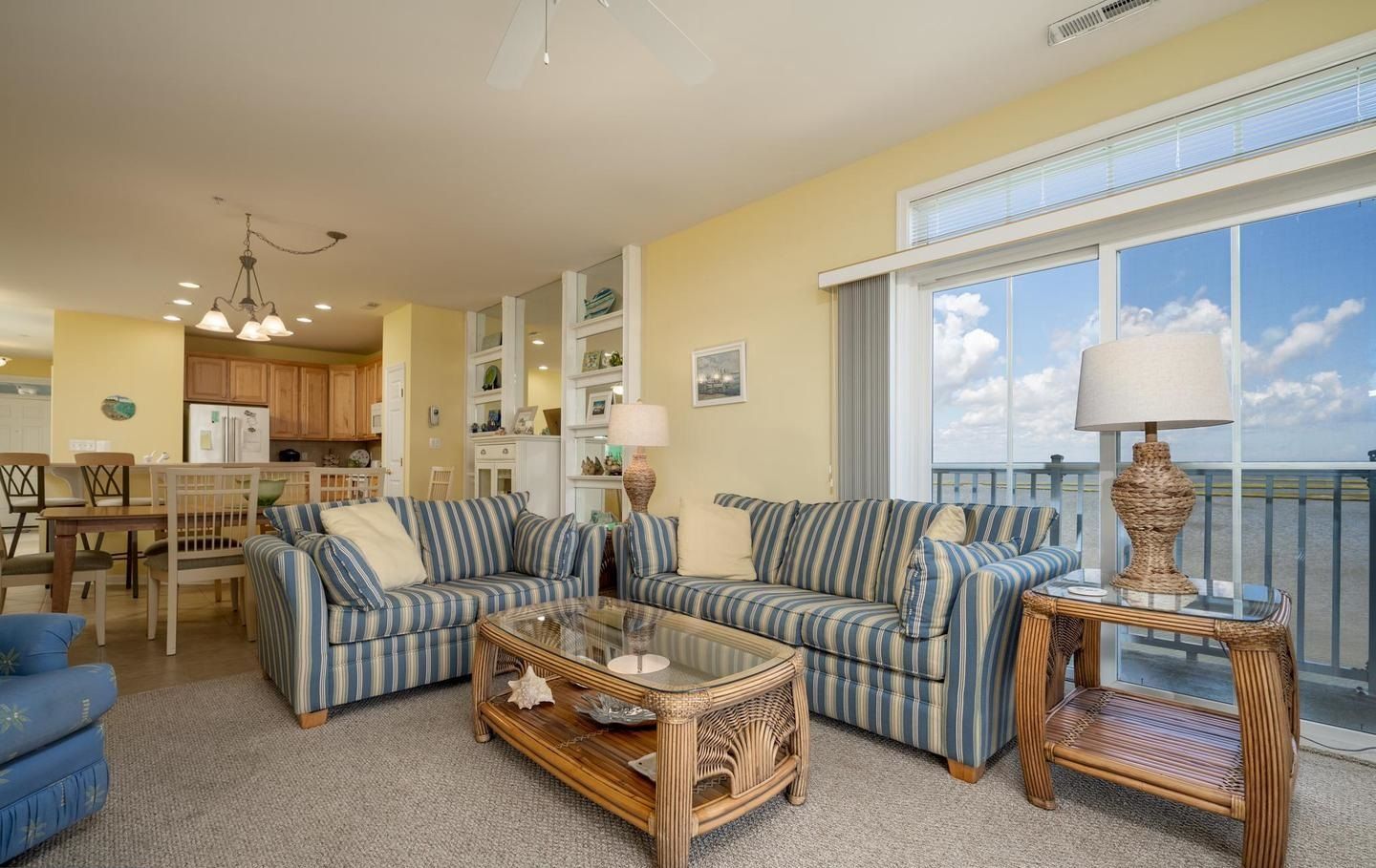 A spacious living room with striped sofas, a glass coffee table, and wicker side tables.