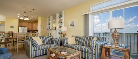 A spacious living room with striped sofas, a glass coffee table, and wicker side tables.