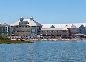Un hotel frente al mar con varias construcciones, una zona de playa con sombrillas y vistas al agua.