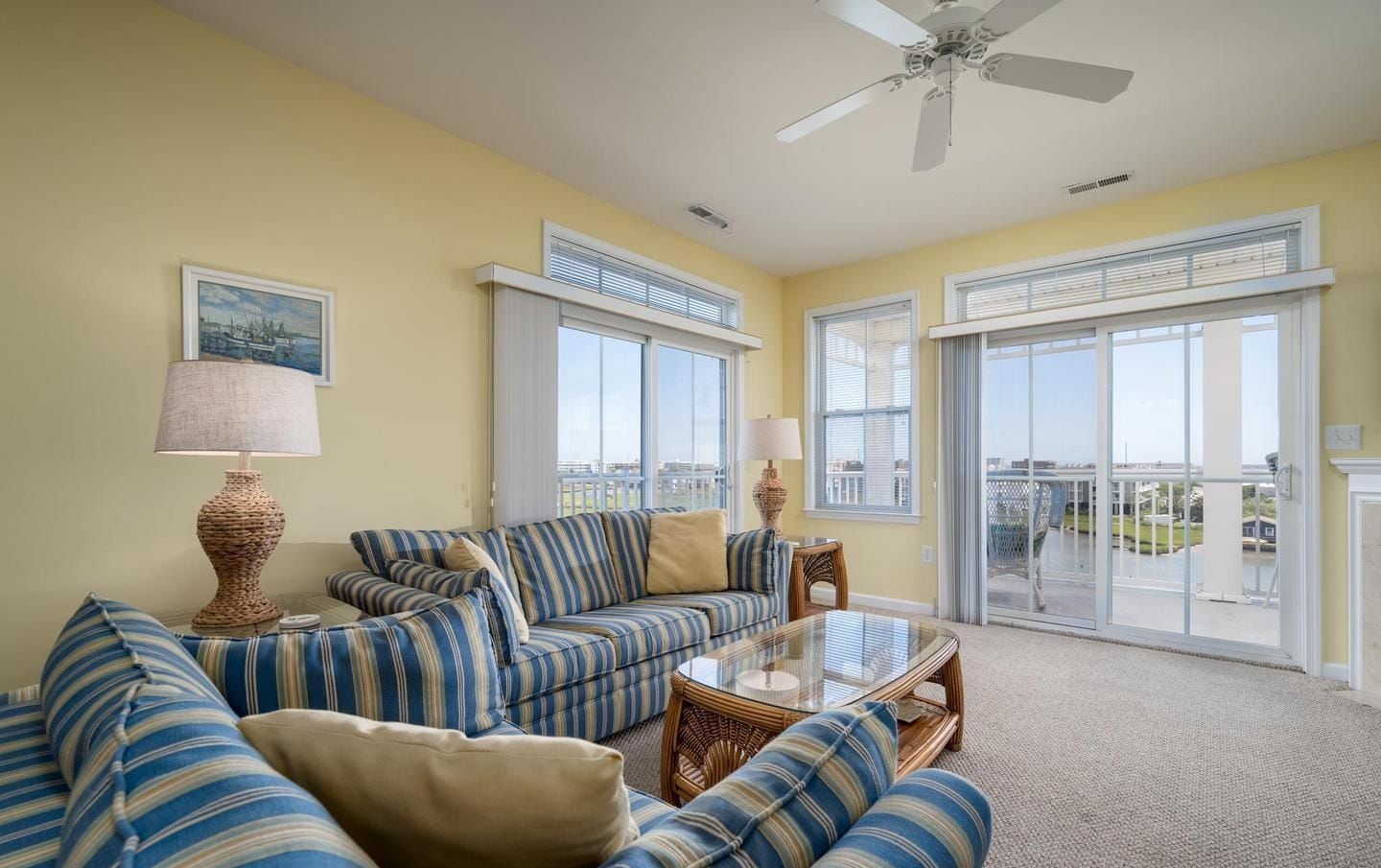 A living room with a sofa set, two lamps, a glass coffee table, and a ceiling fan.