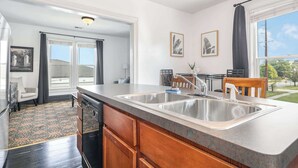 A kitchen with a double sink, wooden cabinets, and a large window. - Spacious 1bd, Close to Beach, Shops, Food & Mall (Michigan City)