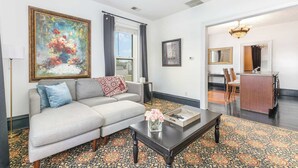 A living room with a sofa, coffee table, and a painting. There is a dining area with a table and chairs. - Spacious 1bd, Close to Beach, Shops, Food & Mall (Michigan City)