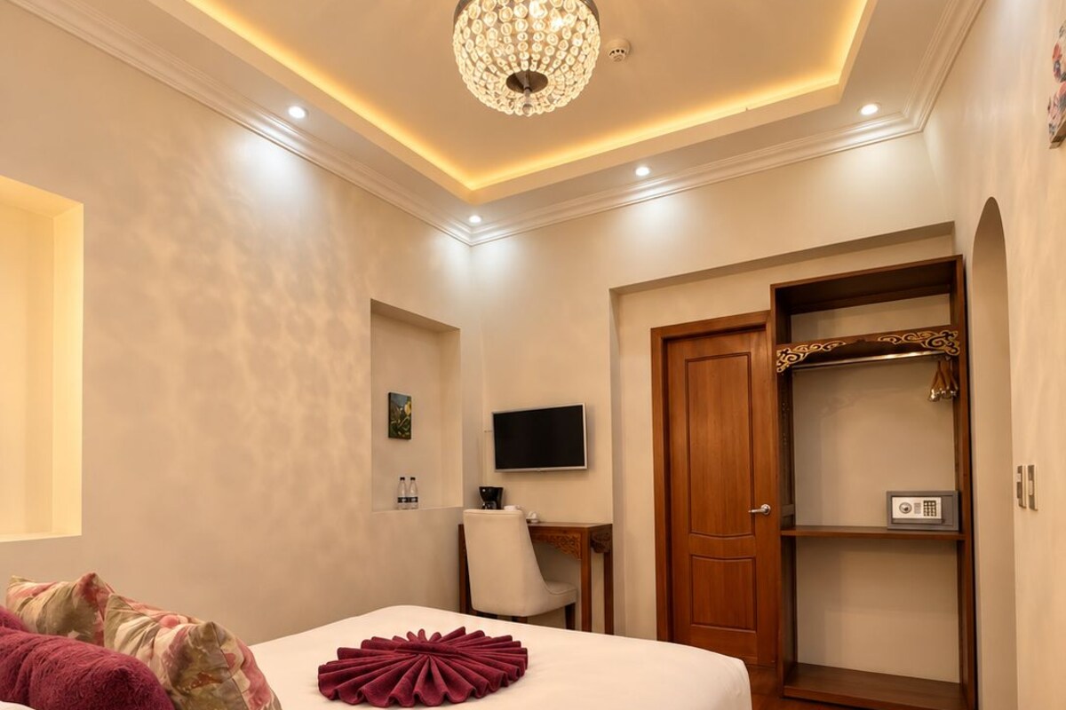A hotel room with a large bed, a television, a wooden wardrobe, and a chandelier.