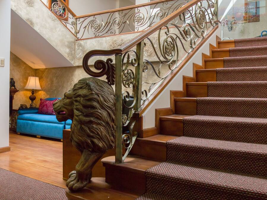 Una escalera con una estatua de león al pie, un sofá azul y una chimenea al fondo.