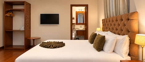 Habitación de hotel con una cama grande, televisión, armario y baño visible a través de una puerta abierta.