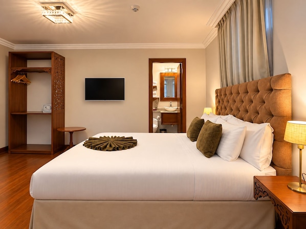 Habitación de hotel con una cama grande, televisión, armario y baño visible a través de una puerta abierta.