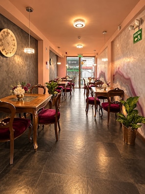 Interior de restaurante con mesas y sillas de madera, pared de mármol y letrero de salida verde.