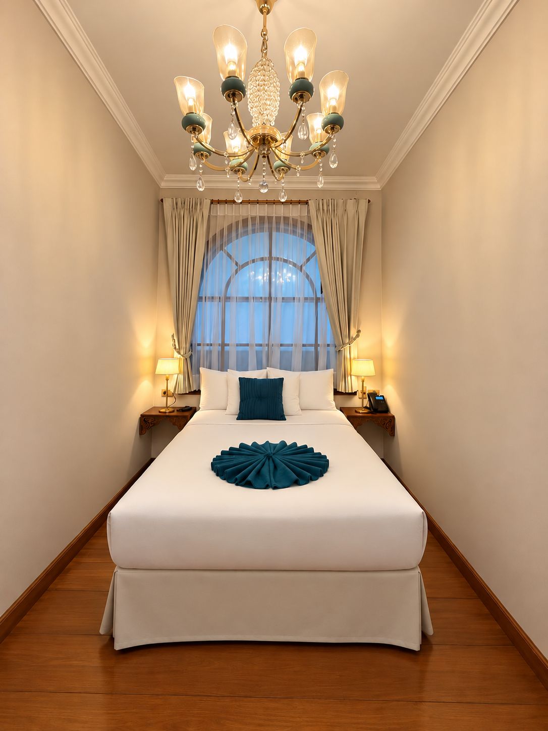 A hotel room with a large bed, a chandelier, curtains, and bedside lamps.