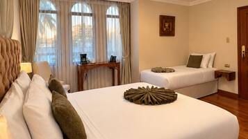 Ein Hotelzimmer mit einem großen Bett, einem kleineren Bett, einem Schreibtisch mit Stuhl und einem fenster mit Vorhängen.